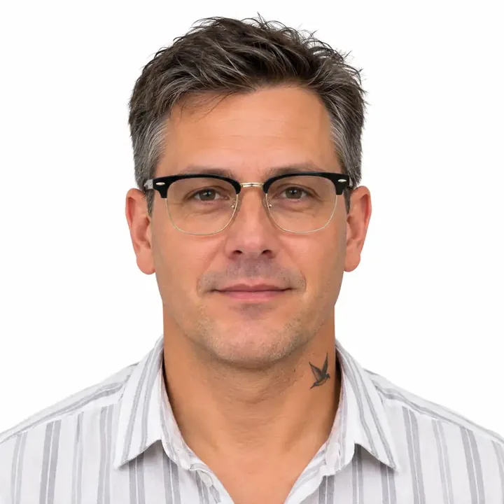 Charles Michael – Roof Guttering Expert Charles Michael wearing round glasses and a white gray striped shirt.