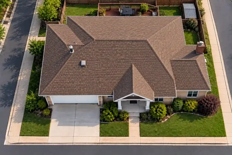 Restored brown shingle roof after storm damage, with clean roofing, intact gutters, and a tidy yard viewed from above.